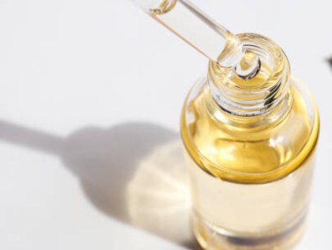 Bottle of cosmetic essential oil and green leaf. Serum oil is dripping from dropper. Close-up. Beauty and body care concept. Serum skin care product. Hard light.